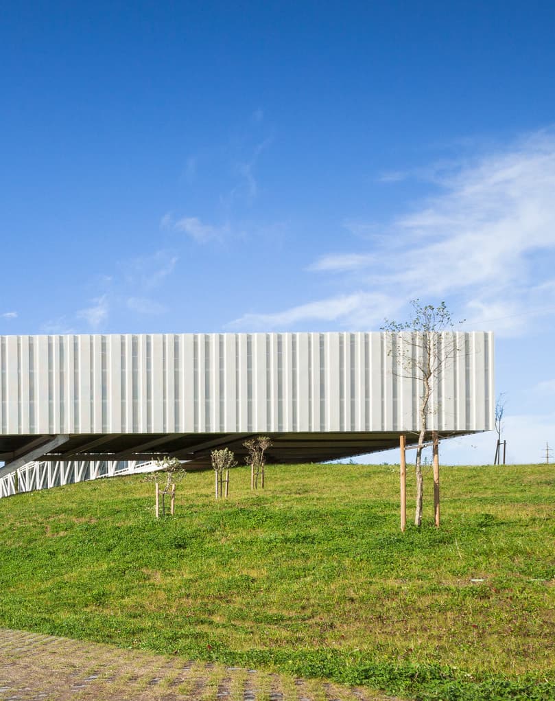 Edifício do Óbidos Parque: uma longa fachada branca sobre uma colina verde, com céu azul